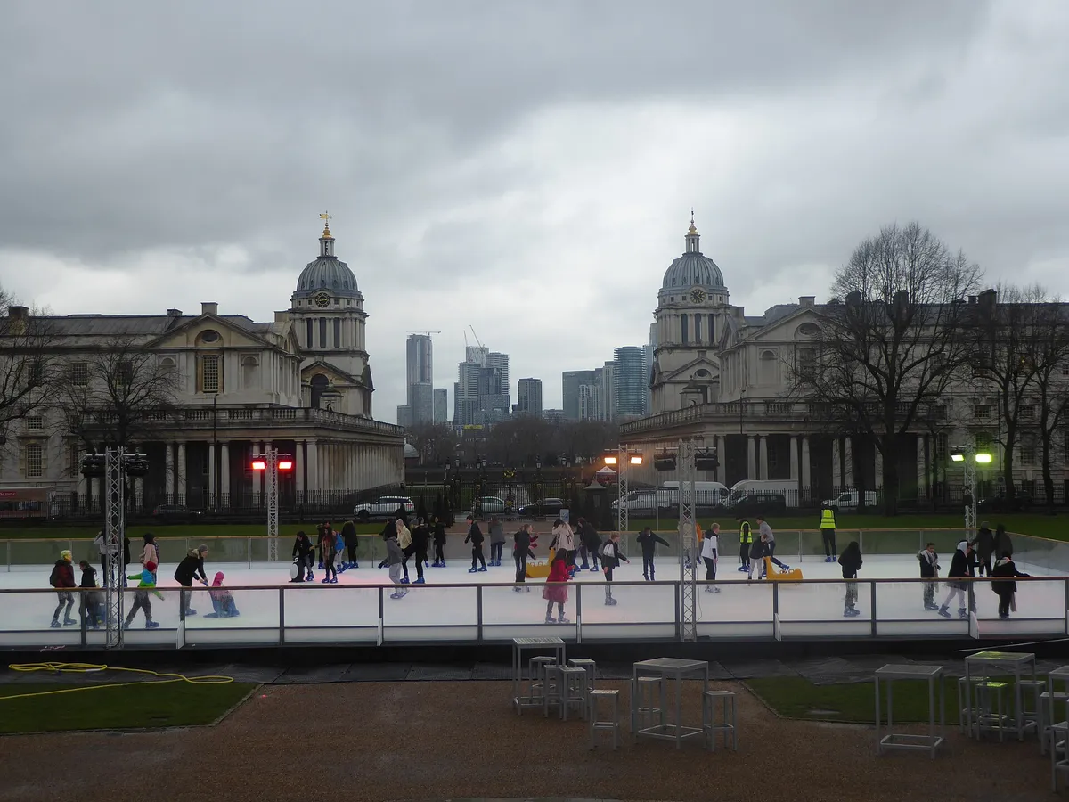 Skaters on an outdoor rink in front of historic domed buildings on an overcast day