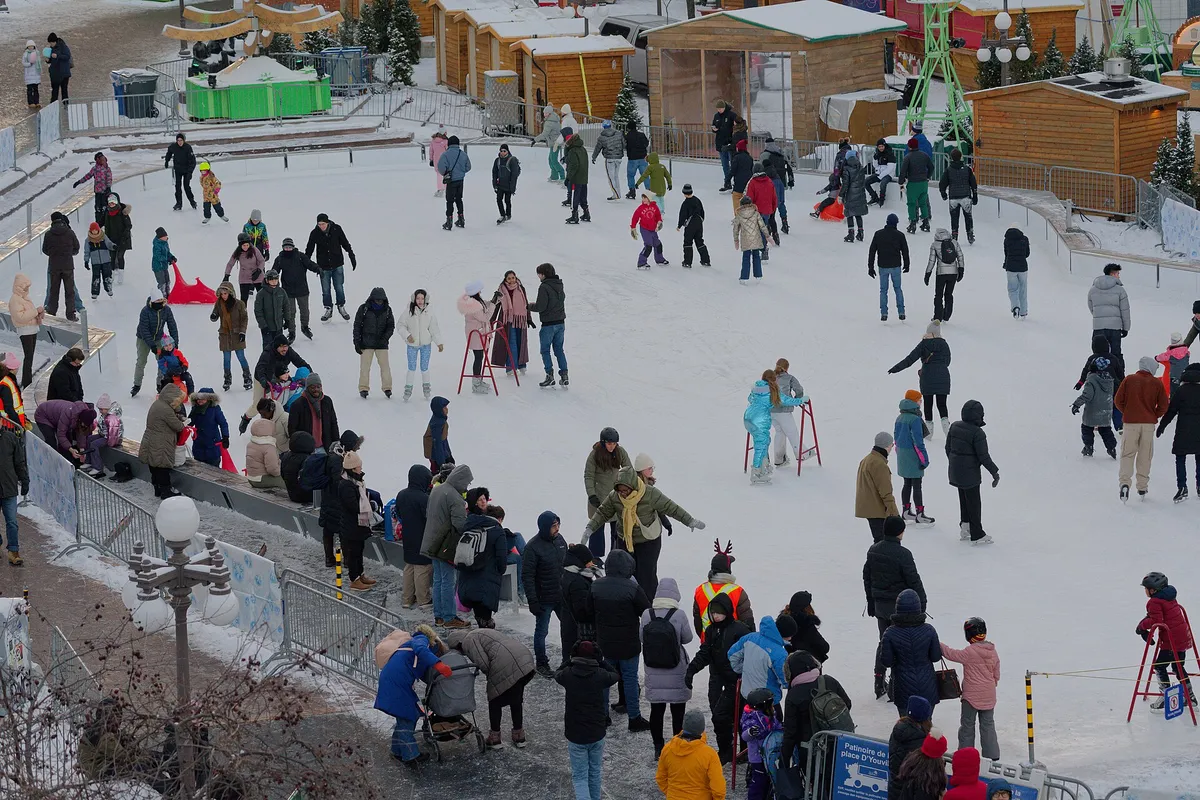 Skaters on an outdoor rink with wooden Christmas market chalets behind