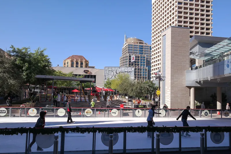 Ice skaters on a sunny outdoor rink in a desert city, downtown towers behind