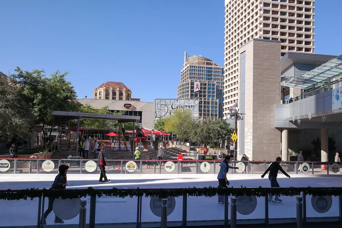 Ice skaters on a sunny outdoor rink in a desert city, downtown towers behind