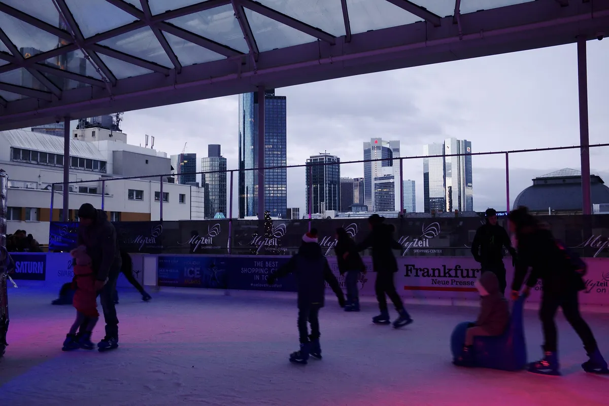 Skaters on an outdoor ice rink in a European city, modern buildings behind