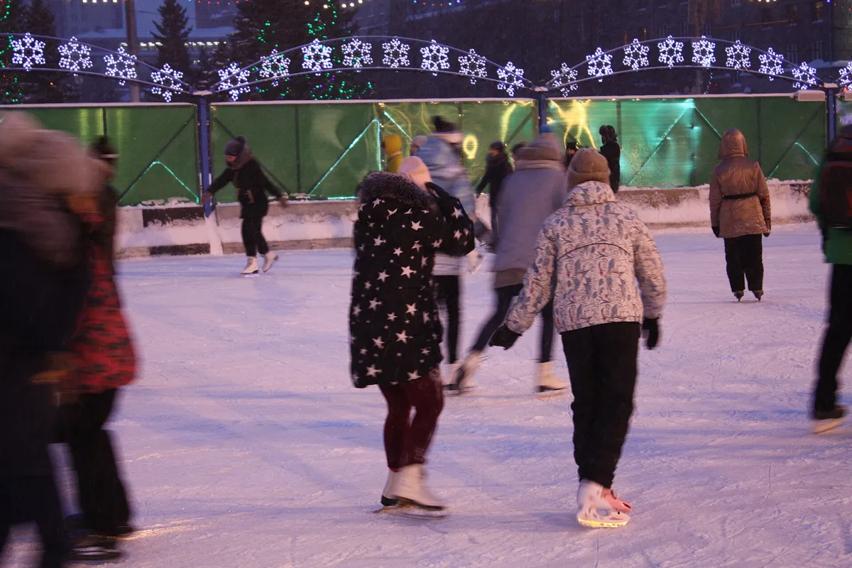 Skaters on an outdoor rink in a large city square, winter coats and hats everywhere