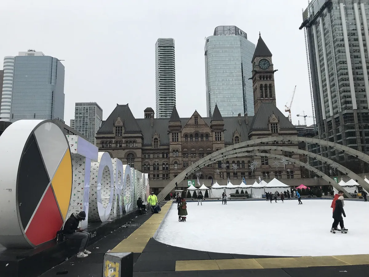 Skaters on an outdoor rink in front of a city hall, towers rising behind