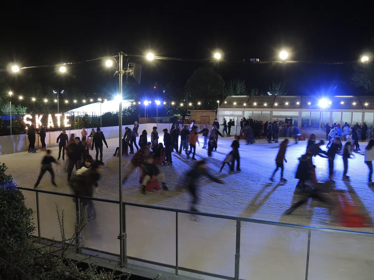 Skaters on an outdoor rink in a historic city, stone buildings around