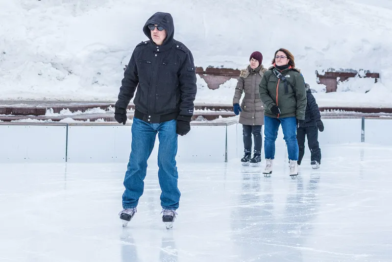 People ice skating outdoors in a city, winter clothes and laughter on the ice