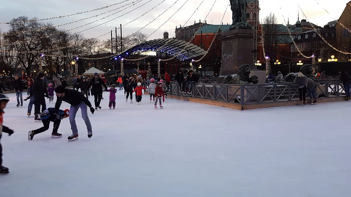 Skaters on an outdoor ice rink in a marketplace, stalls and winter light