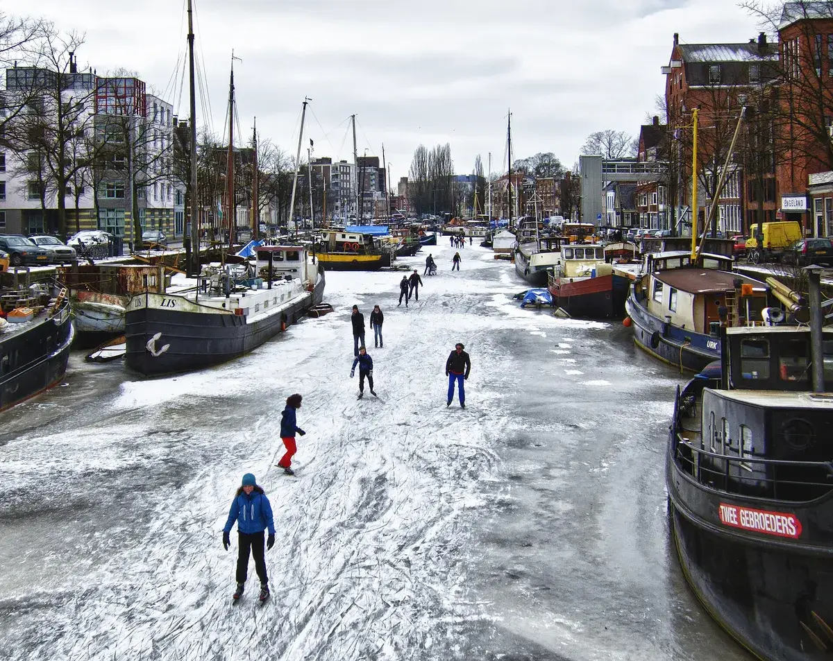 People skating on a frozen canal between moored boats in a city