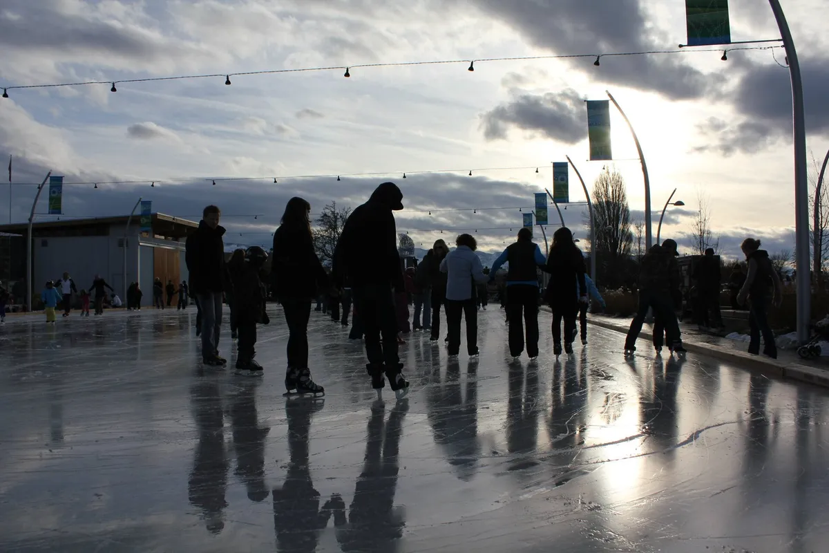 Skaters on an outdoor park rink, mountains and winter sky in the distance