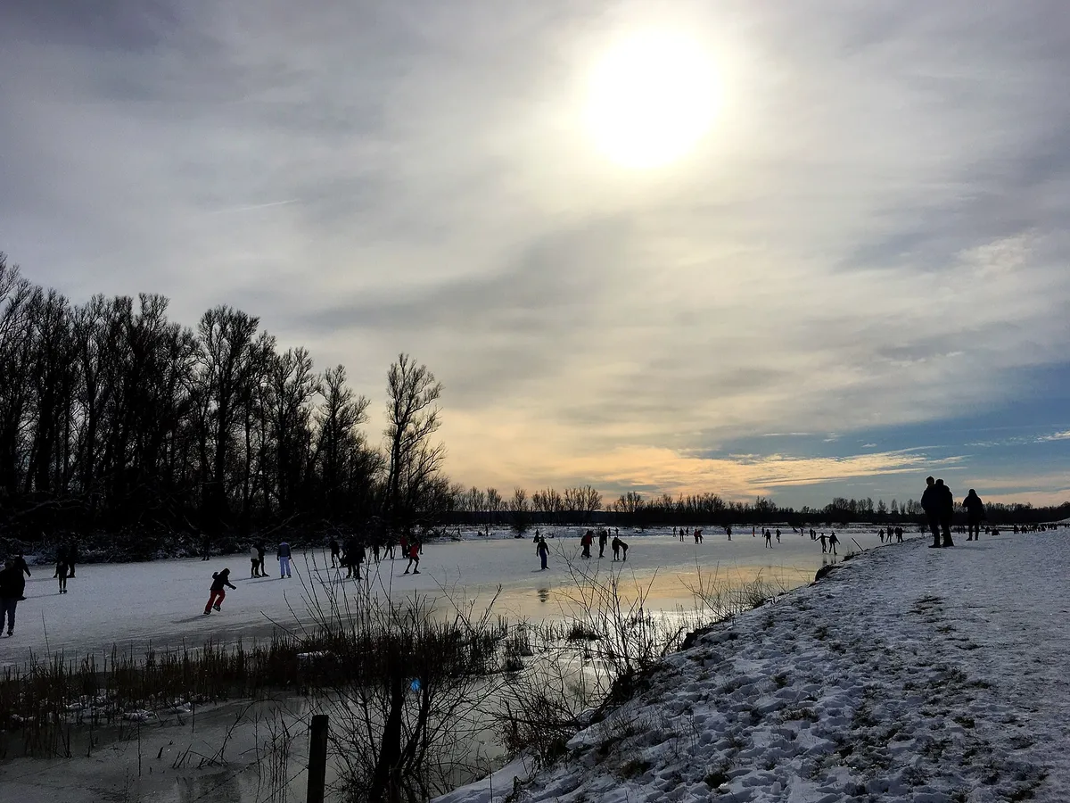 Skaters on a frozen river in a winter landscape, trees lining the banks
