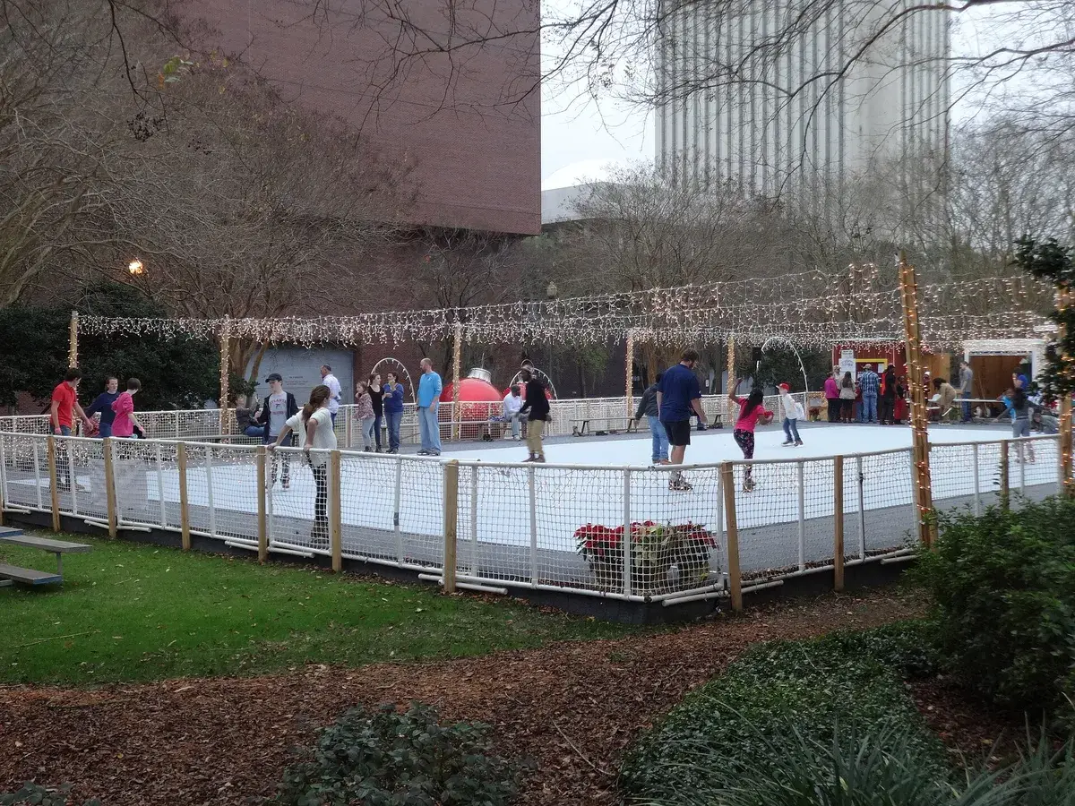 An outdoor rink glowing with Christmas lights, skaters circling after dark