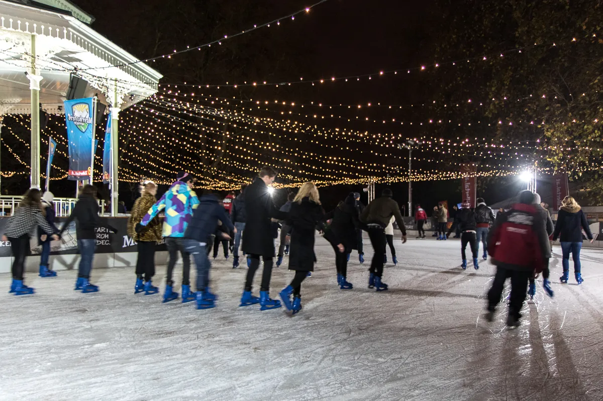 Skaters gliding under strings of lights on an outdoor rink at night